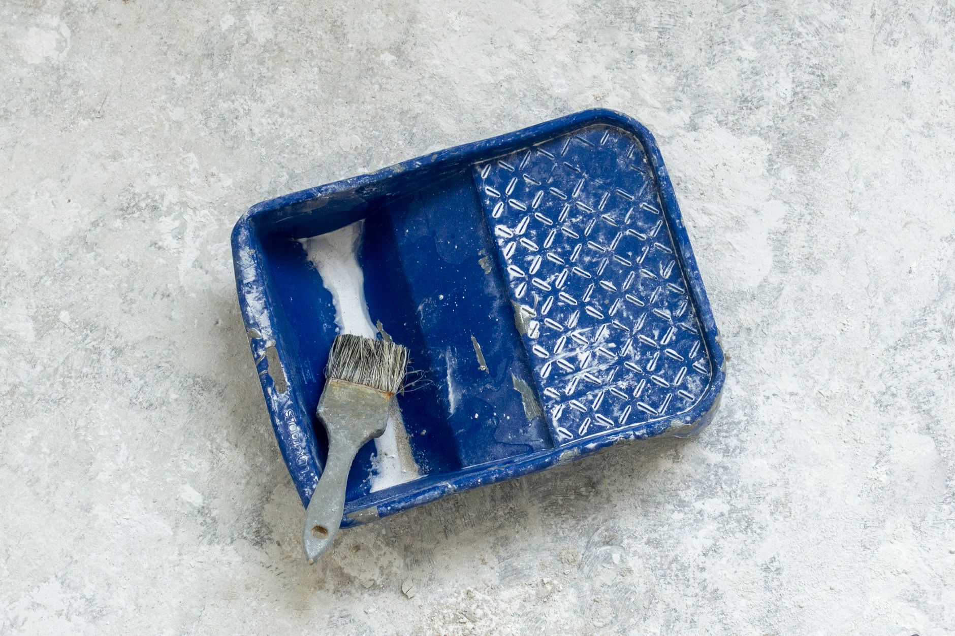 Stock photo of a well-used blue paint tray and brush on a textured surface, perfect for renovation themes