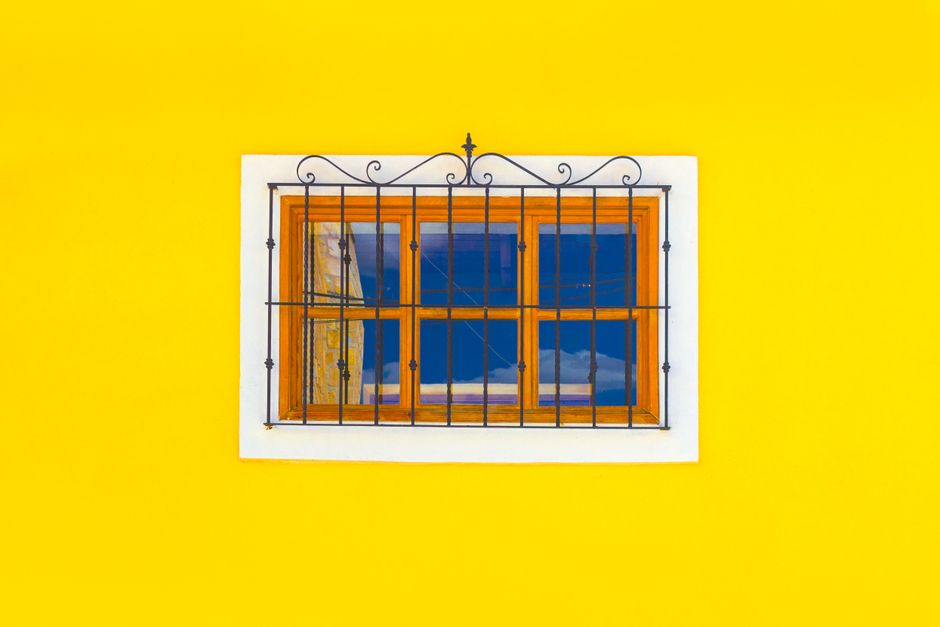 A small window with a wooden frame set in a yellow painted wall